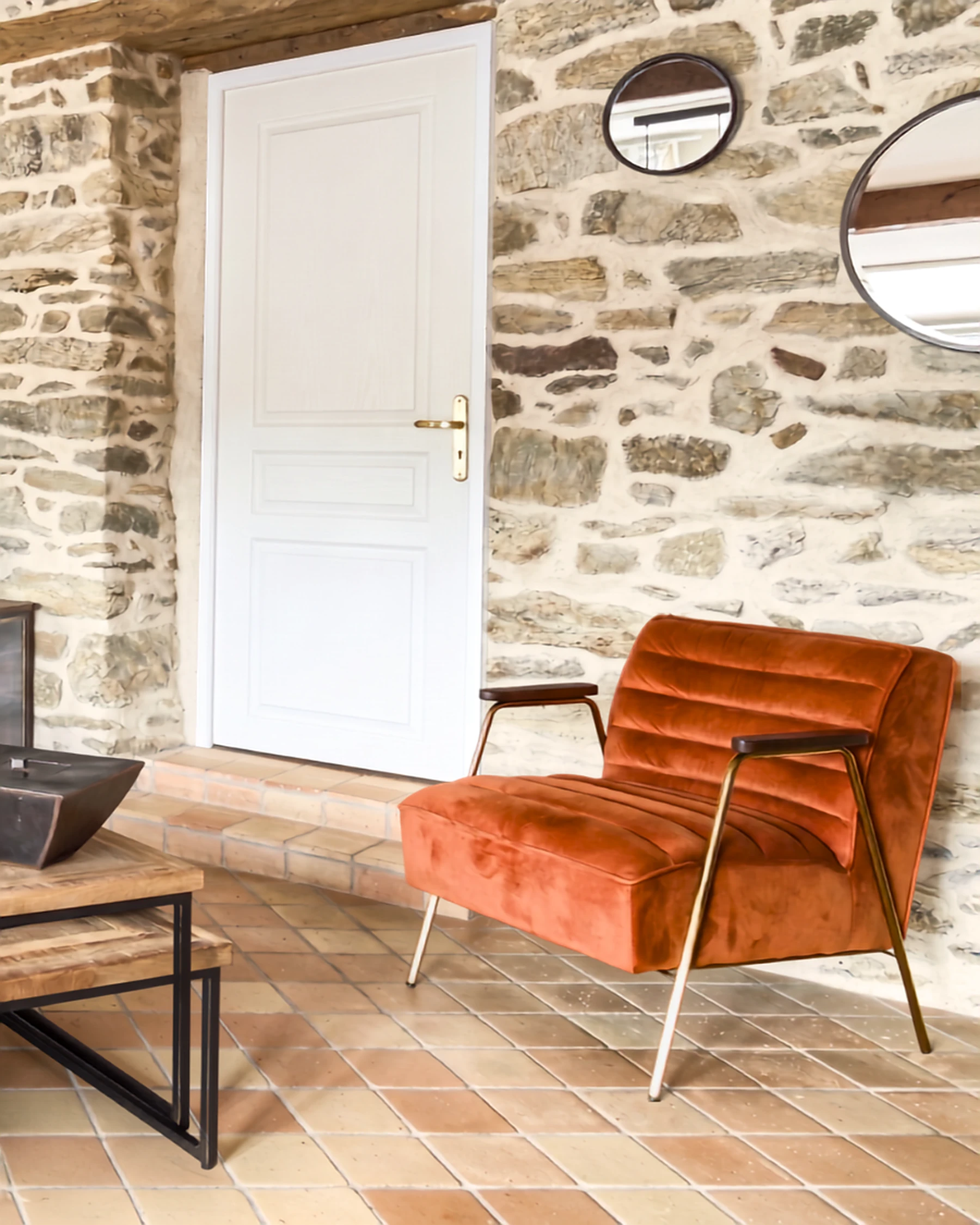 Entrée d'une maison ancienne en pierre, fauteuil terracotta et sol en tomettes